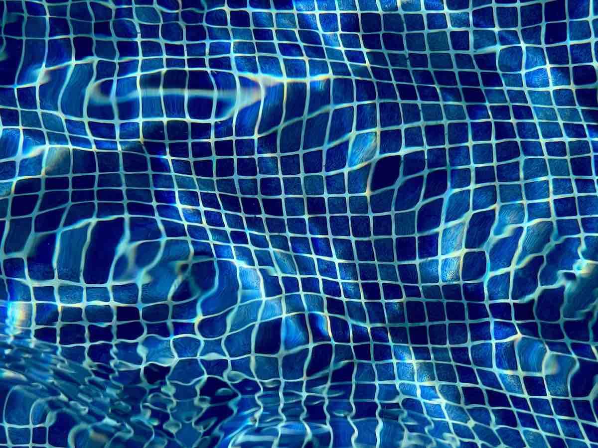 Blue mosaic pool tiles under water in swimming pool.