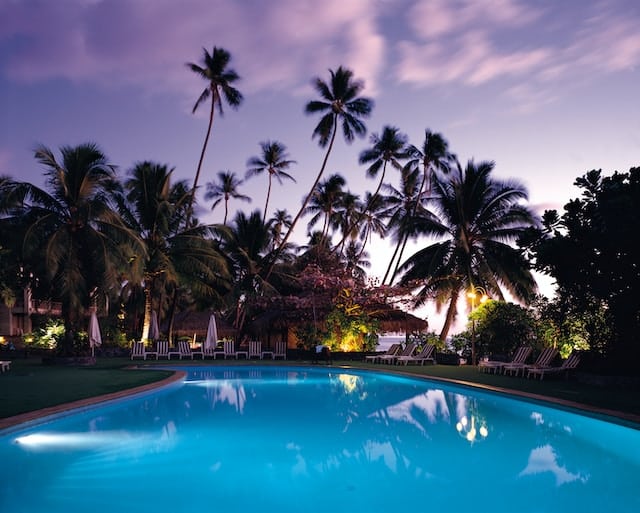 Blue outdoor swimming pool with palm trees in the background. Take advantage of some of the benefits of running your pool pump at night. Photo by Raining Huang.